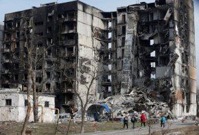 Местни жители се разхождат край разрушена жилищна сграда в обсадения южен пристанищен град Мариупол, Украйна, на 30 март. (Александър Ермоченко/Reuters)