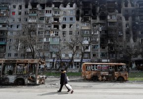 Местен жител върви по улица покрай разрушени автобуси и сгради в южния пристанищен град Мариупол, Украйна, на 19 април. (Александър Ермоченко/Reuters)