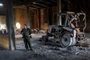 Украинският селскостопански работник Миша стои до трактор, разрушен от руски танков снаряд на 14 май в Черска Лозова, Украйна