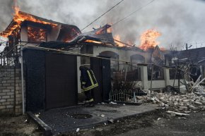Пожарникар стои до горяща къща, пострадала от руския обстрел в Херсон, Украйна, навръх православната Коледа, 6 януари. (LIBKOS/AP)