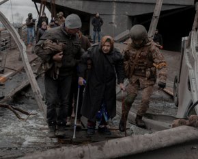 На възрастна жена се оказва помощ, докато преминава през разрушен мост, докато се опитва да напусне град Ирпин в Киевска област, Украйна, март