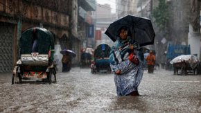 Жена държи чадър, докато върви по наводнена улица по време на проливен дъжд в Дака, Бангладеш, през юни.